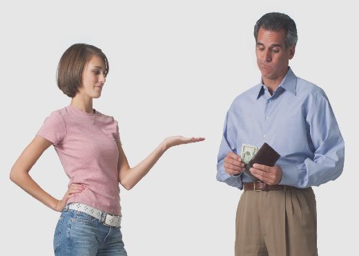 a caucasian teenage girl puts out her hand as her father pulls out his wallet to give her money