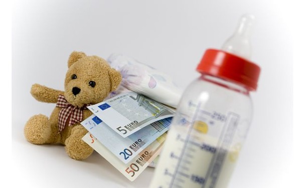 Ein Stapel Babywindeln, Schoppen,Teddybär und Geldscheine vor weißem Hintergrund